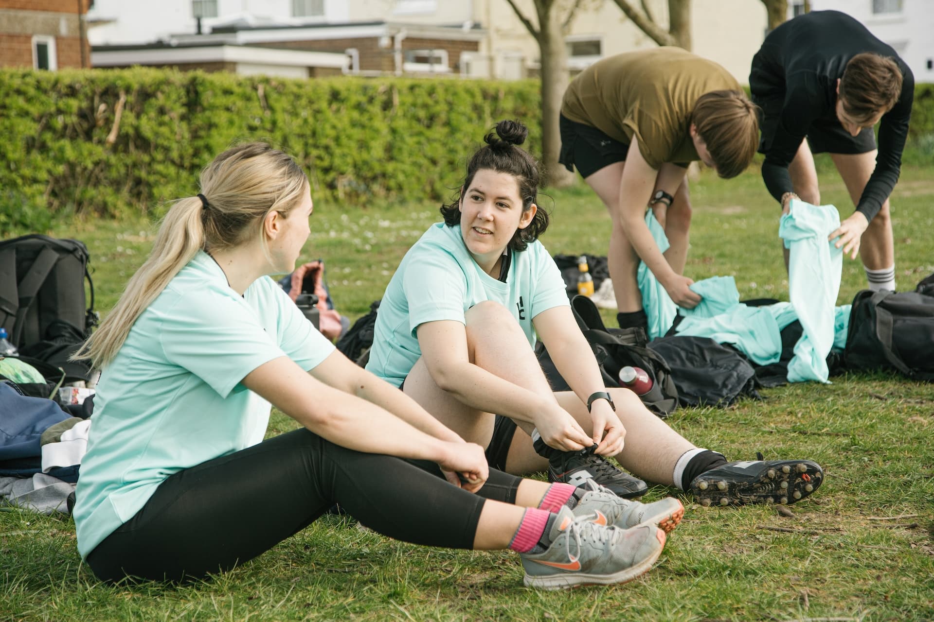 Teammates sitting on the grass pulling their boots on